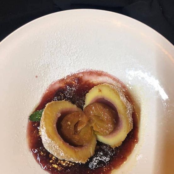 Ein Teller mit zwei Dessertrollen gefüllt mit einer süßen Füllung, überzogen mit Puderzucker und einer roten Beerensauce.