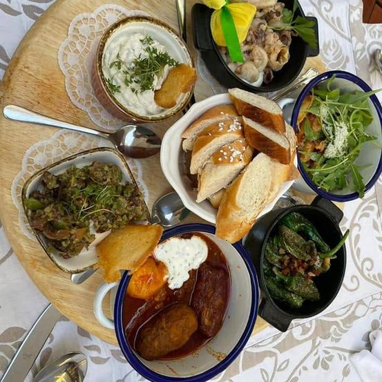 Ein hölzerner Tisch zeigt eine Auswahl an Gerichten, darunter eine Schüssel mit cremiger Dip, eine Schüssel mit Brot und eine Schüssel mit grünem Gemüse.