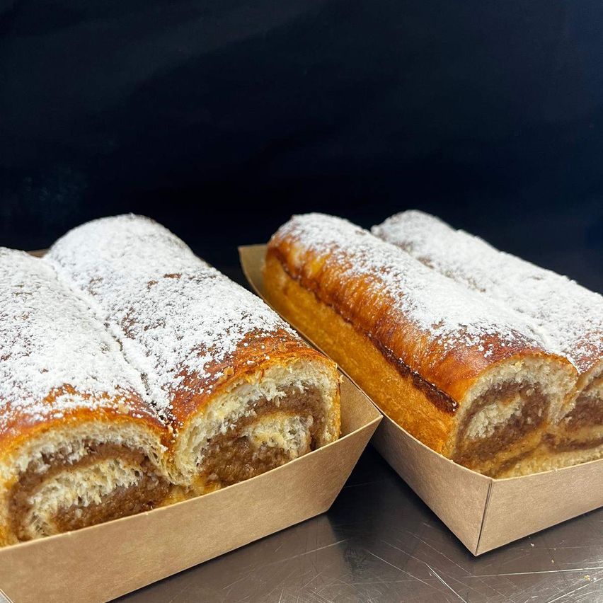 Two boxes of rolled pastries with a brown and white filling, dusted with powdered sugar, on a metallic surface.