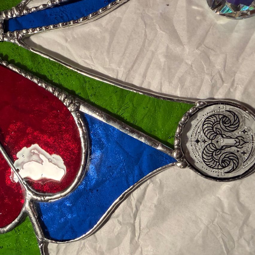 Ein Buntglasstück mit roten, blauen und grünen Farben, mit silbernem Rahmen und einem dekorativen Design auf der rechten Seite.