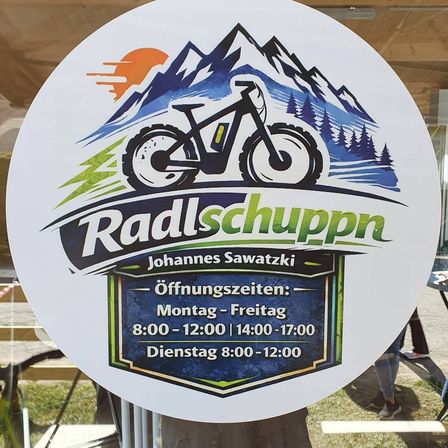 Ein rundes Schild mit dem Text Radlschuppen und einem Fahrradlogo. Die Öffnungszeiten sind Montag bis Freitag von 8:00-12:00, 14:00-17:00.