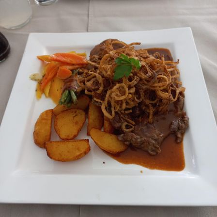 Ein Teller mit Steak, Soße, knusprigen Zwiebeln und Gemüse, darunter Kartoffeln, Karotten und grüne Bohnen.