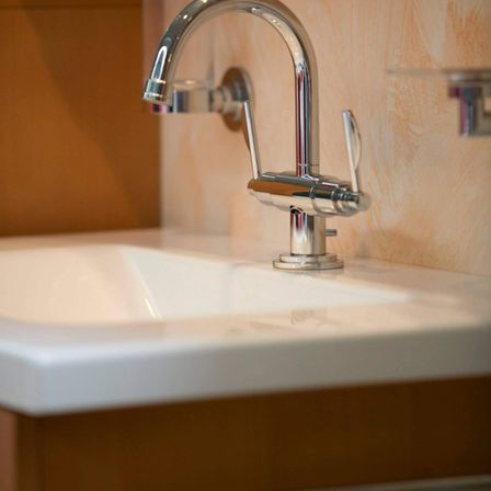 Ein modernes Badezimmer mit einem Chrom-Wasserhahn und einer beigen Wand. Das Waschbecken ist sauber und glänzend.