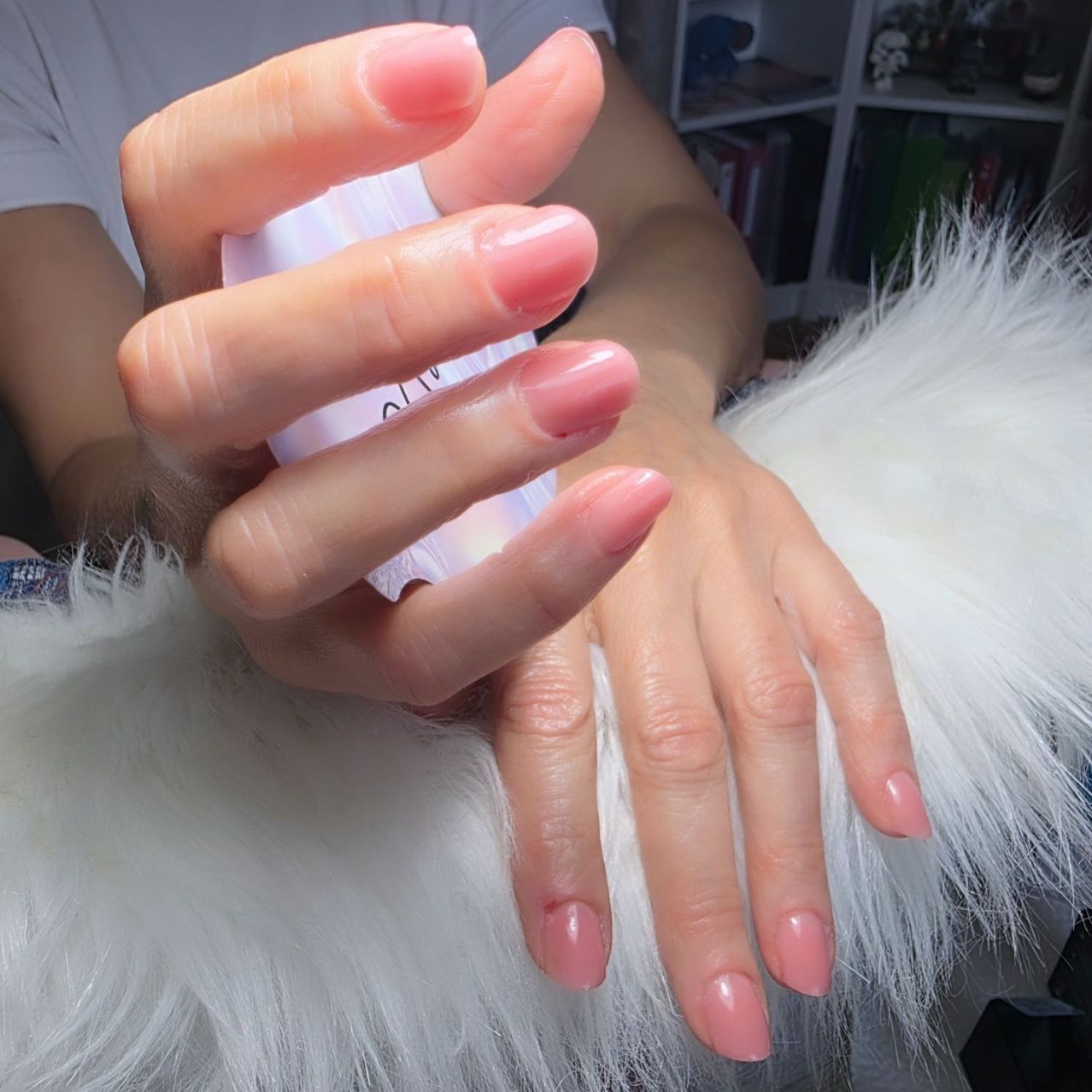 Eine Person hält eine Flasche Nagellack und zeigt ihre frisch lackierten Nägel auf einer weißen pelzigen Oberfläche.