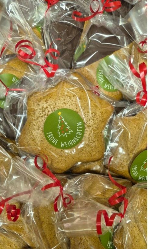 Eine Nahaufnahme von Keksen in Plastikverpackung, jeweils in einem roten Band verpackt, wobei einige Kekse ein grünes Etikett haben, das 'Frohe Weihnachten' besagt.