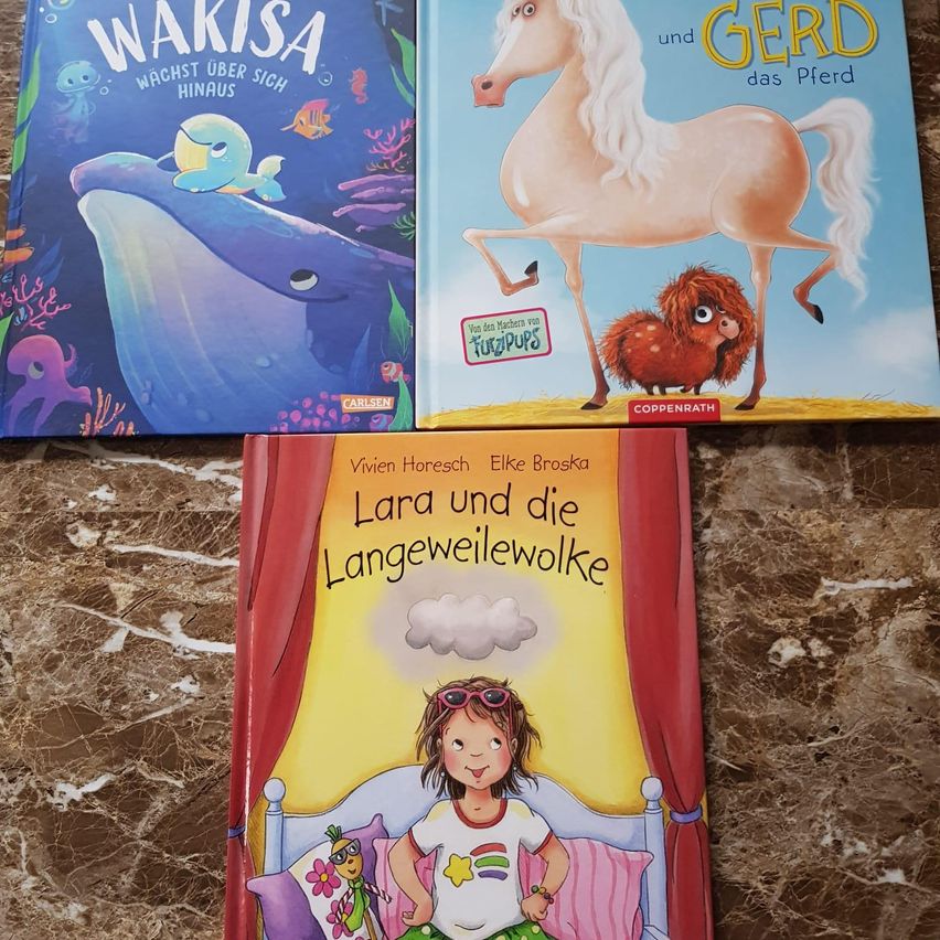 Drei Bücher liegen auf einer Marmoroberfläche. 'Wakisa' zeigt einen Wal mit einem Fisch. 'Gerd' zeigt ein Pferd und ein kleines Tier. Darunter befindet sich 'Lara und der Langeweilewolf' mit einem Mädchen im Bett mit Spielzeug.