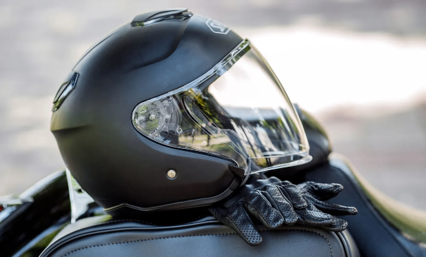 Ein schwarzer Motorradhelm mit klarem Visier ruht auf einem Ledersitz, begleitet von einem Paar schwarzen Handschuhen.