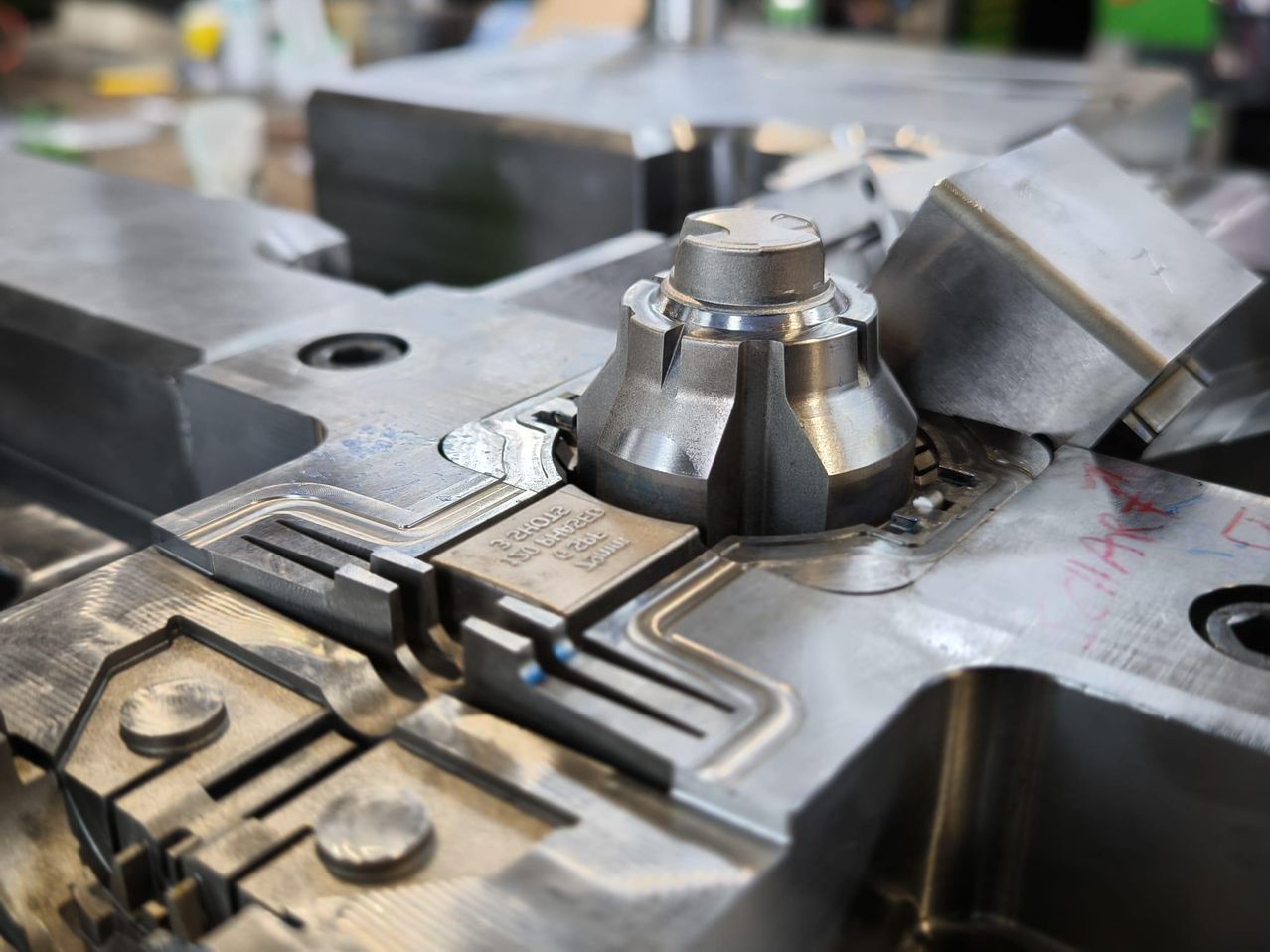 Eine Nahaufnahme eines metallischen Maschinenteils, das ein zylindrisches Objekt mit einer Reihe von Rillen und einer gravierten Beschriftung zeigt. Es ist von anderen Maschinenteilen und Metallkomponenten umgeben.