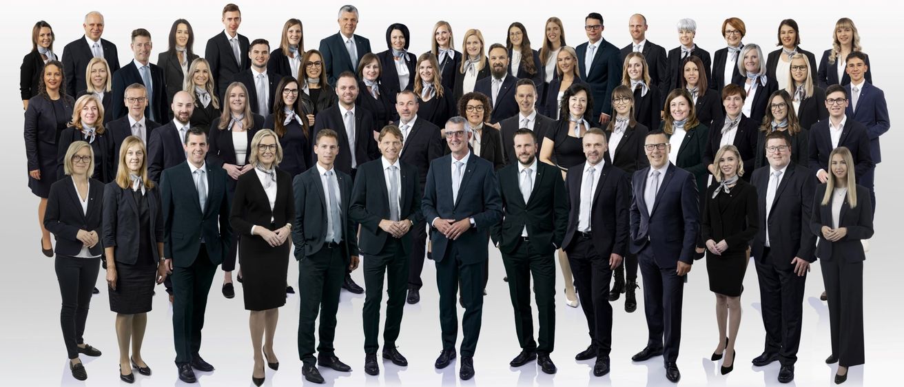 Eine Gruppe von Menschen in formeller Kleidung steht in einer Reihe und posiert für ein Foto. Sie tragen alle Krawatten und einige von ihnen tragen Brillen.