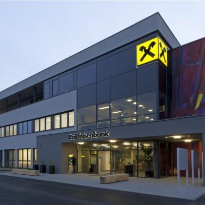 Ein modernes Bankgebäude mit einem gelben Schild mit X-Logo, großen Glasfenstern und einem Eingang mit Doppeltüren und einer Bank.