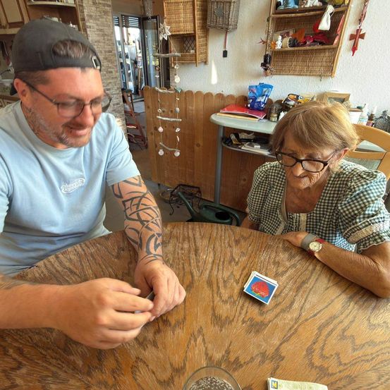 Ein Mann und eine Frau sitzen an einem Holztisch, lächeln und schauen sich eine Karte an. Der Mann hat Tattoos am Arm.