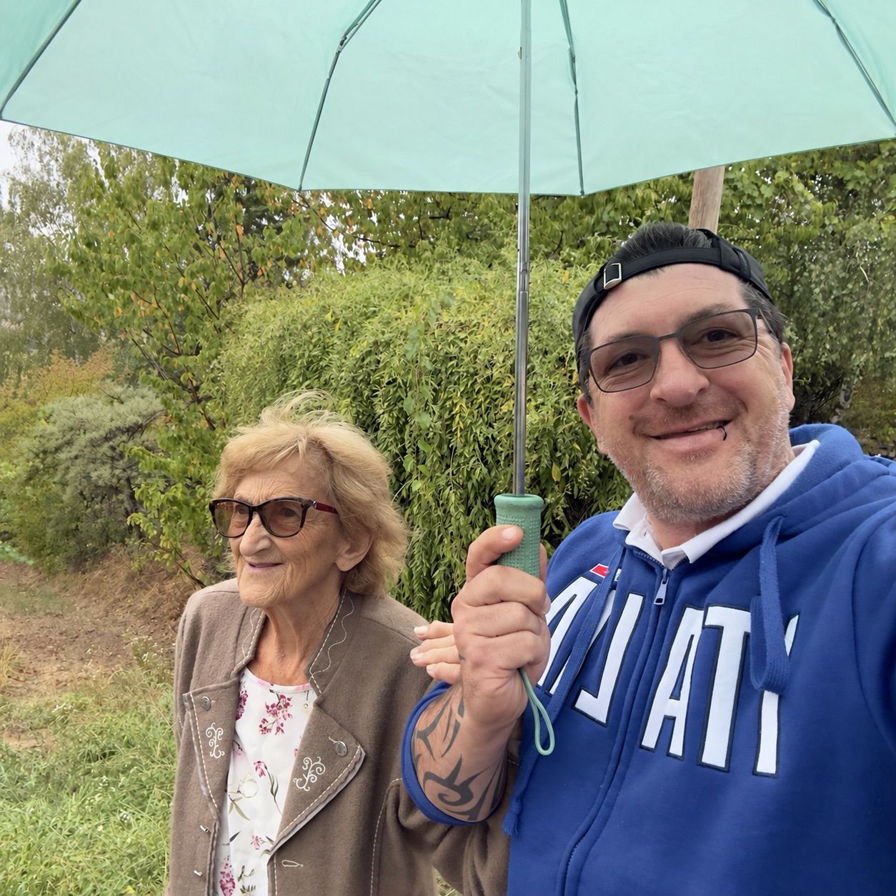 An elderly woman and a man are smiling and holding a green umbrella in a park.