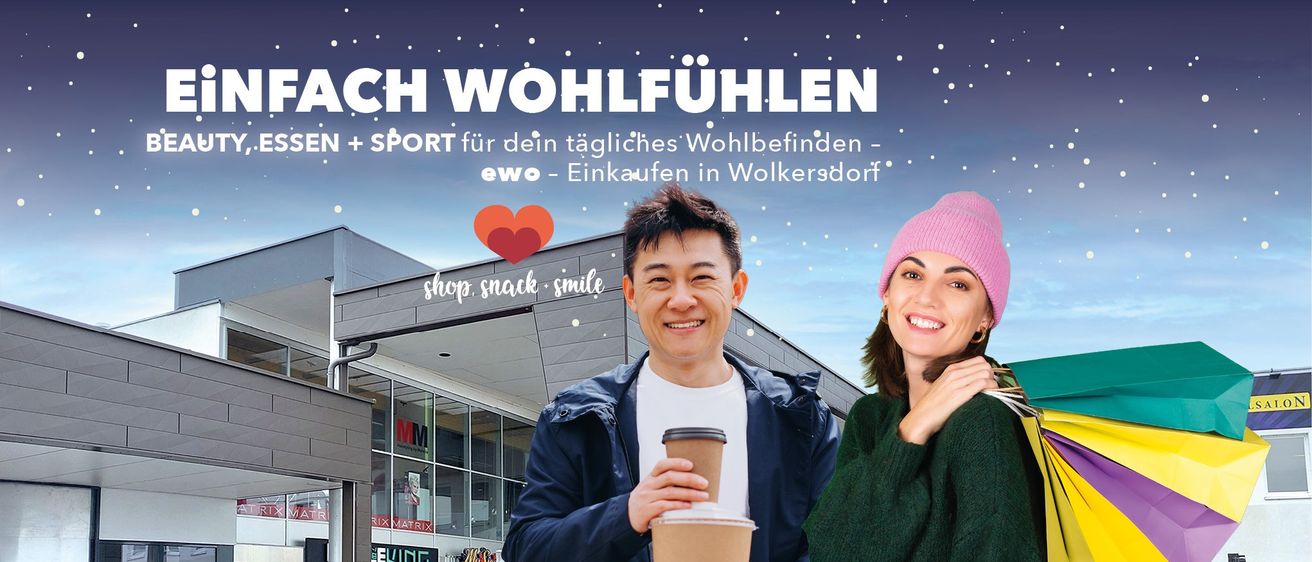 Zwei lächelnde Personen stehen vor einem Geschäft, eine hält einen Kaffee. Der Himmel ist blau mit weißen Schneeflocken. In der Mitte befindet sich ein rotes Herz. Das Geschäft hat Glaswände und Displays. Der Text lautet 'CH WOHLFÜHLEN SPORT für dein tägliches Wohlbefinden - ewo - Einkaufen in Wolkersdorf'.