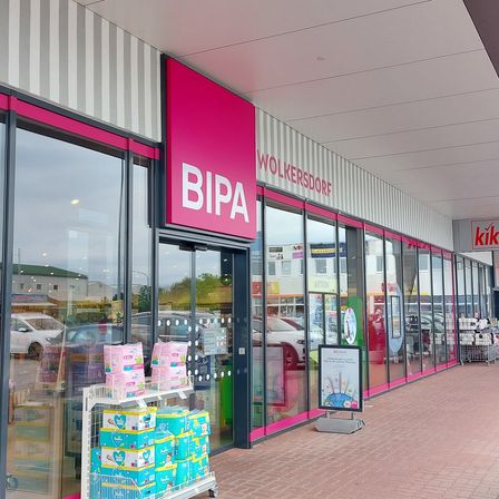 Ein BiPA-Geschäft in einer Straße mit einem Parkplatz davor. Das Geschäft hat Glaswände und eine Glastür.