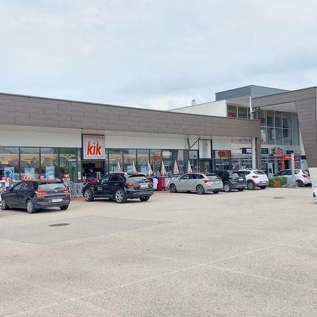 Außenansicht eines Einkaufszentrums mit einem großen KIK-Geschäft und mehreren Autos davor.