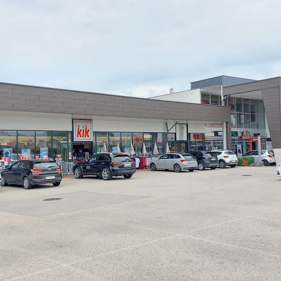 Außenansicht eines Einkaufszentrums mit einem großen KIK-Geschäft und mehreren Autos davor.
