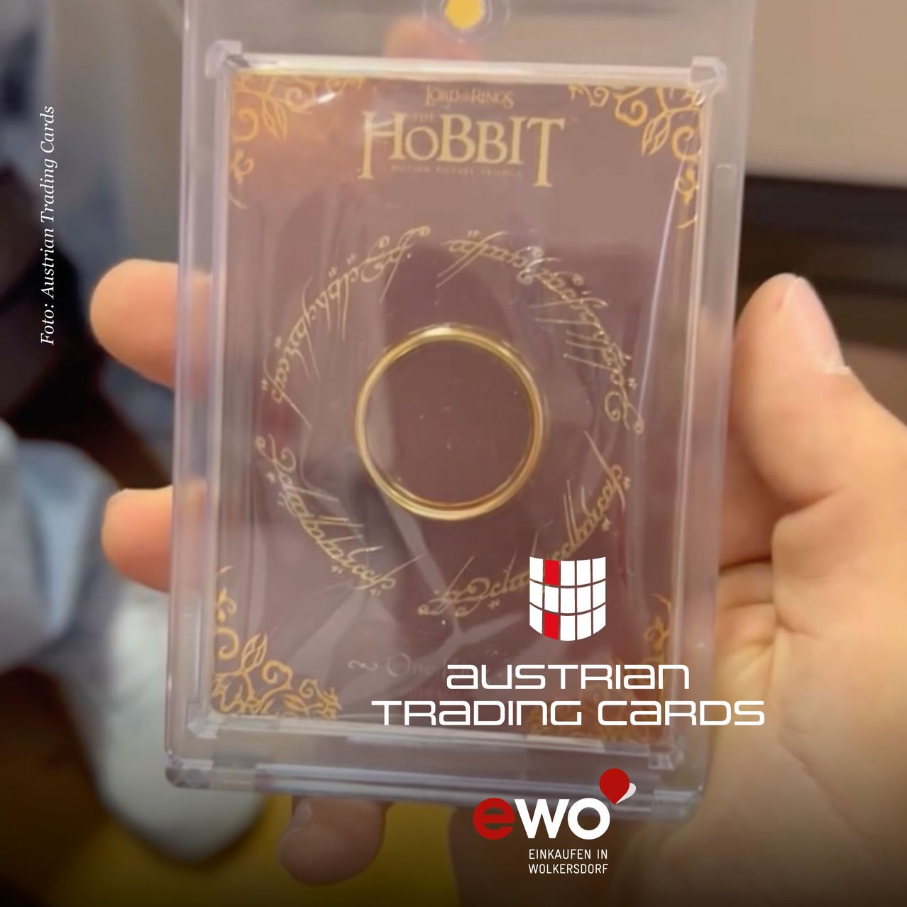 Eine Person hält eine durchsichtige Plastikhülle mit einem goldenen Ring darin. Der Ring befindet sich mittig und die Hülle hat ein Design mit den Worten 'Der Hobbit' und einem Logo.
