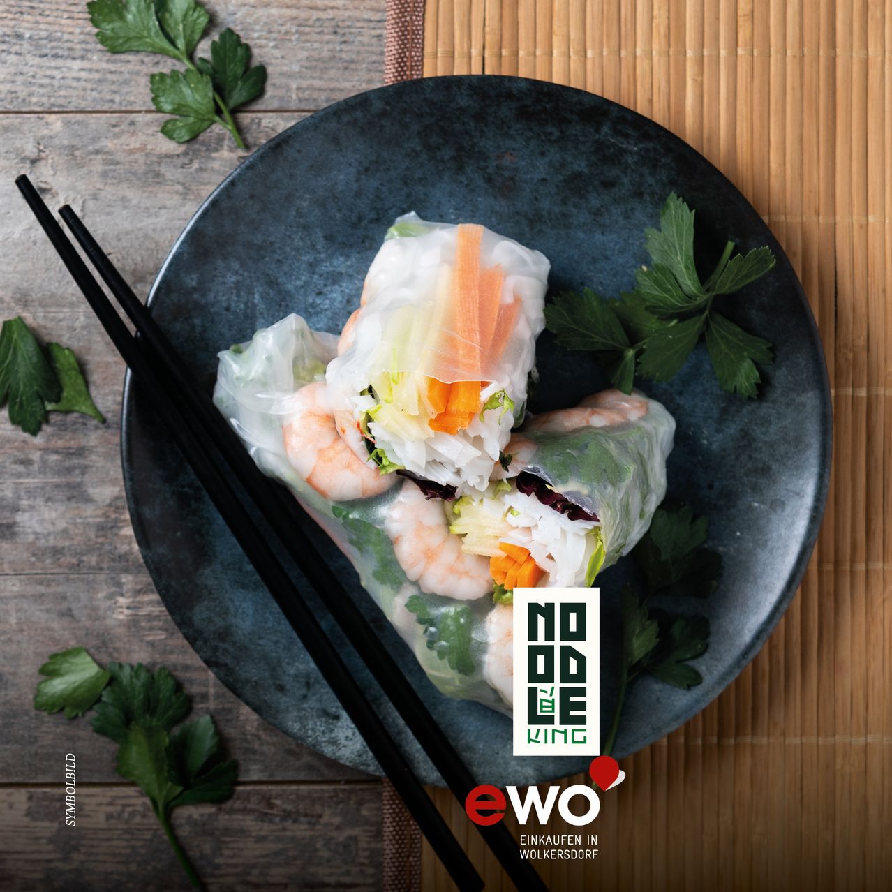 Ein Teller mit Reispapierrollen mit Garnelen, Gemüse und Kräutern, serviert mit Chopsticks auf einer Bambusmatte.