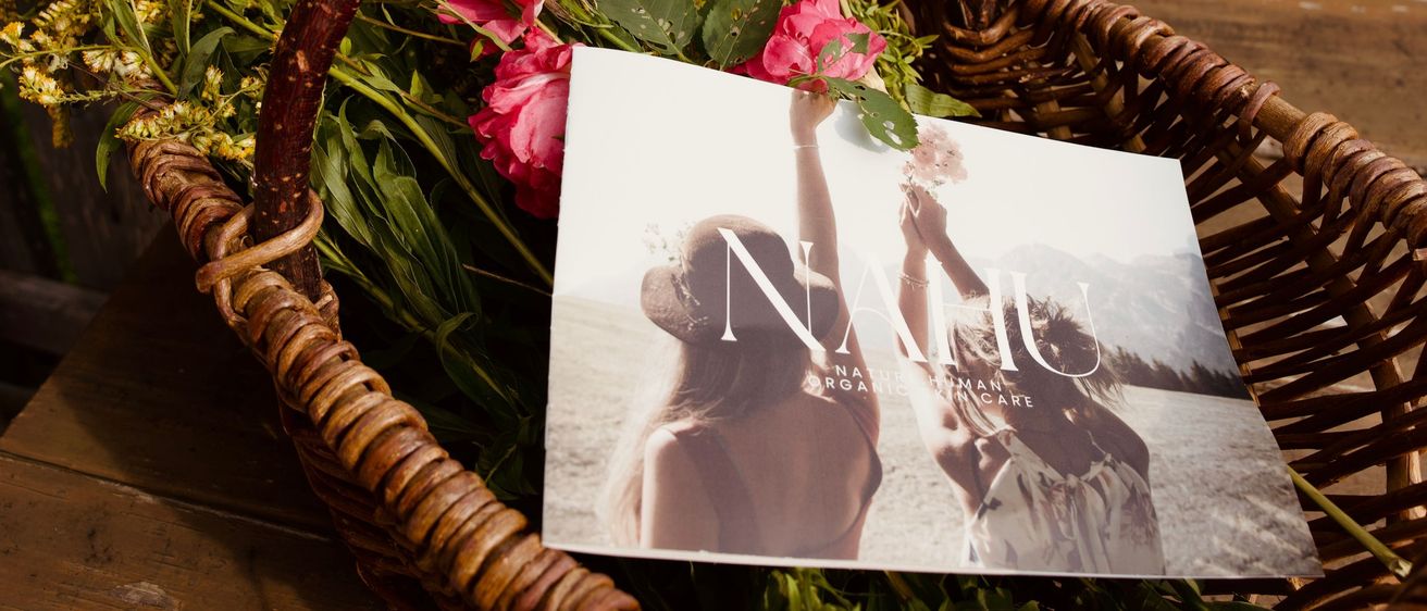 Ein Korb mit gelben und rosa Blumen auf einem Holztisch. Ein Bild von zwei Frauen, die Blumen halten, ist im Korb platziert.