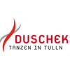 Das Logo für Duschek Tanzen in Tulln, mit einer stilisierten roten Flamme und grauen Umrissen. Das Wort 'Duschek' ist in fetten roten Buchstaben über der Flamme geschrieben, während 'Tanzen in Tulln' in kleineren grauen Buchstaben darunter steht.