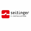 Ein rotes quadratisches Logo mit weißem Pfeil und Text 'seitinger E-INSTALLATION' auf weißem Hintergrund.