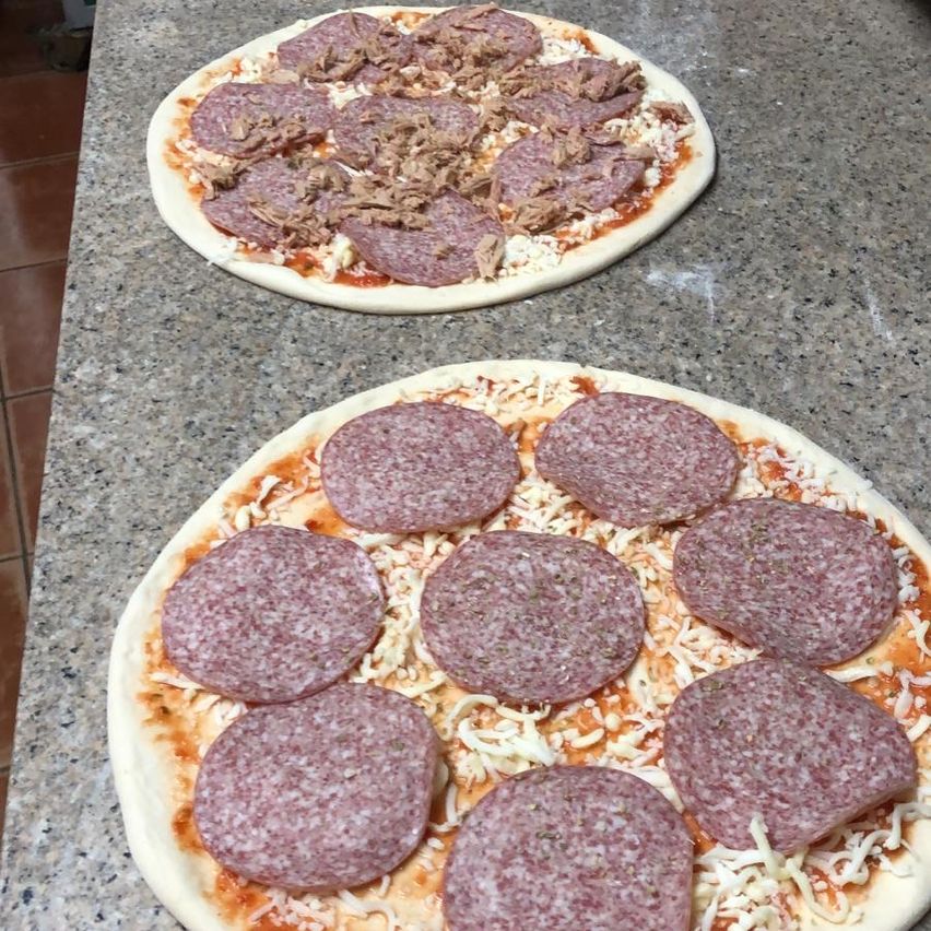 Zwei Pizzen auf einem Tisch, eine mit Peperoni und eine andere mit einer Mischung aus Peperoni und Wurst auf einem roten Tomatensaucenboden.