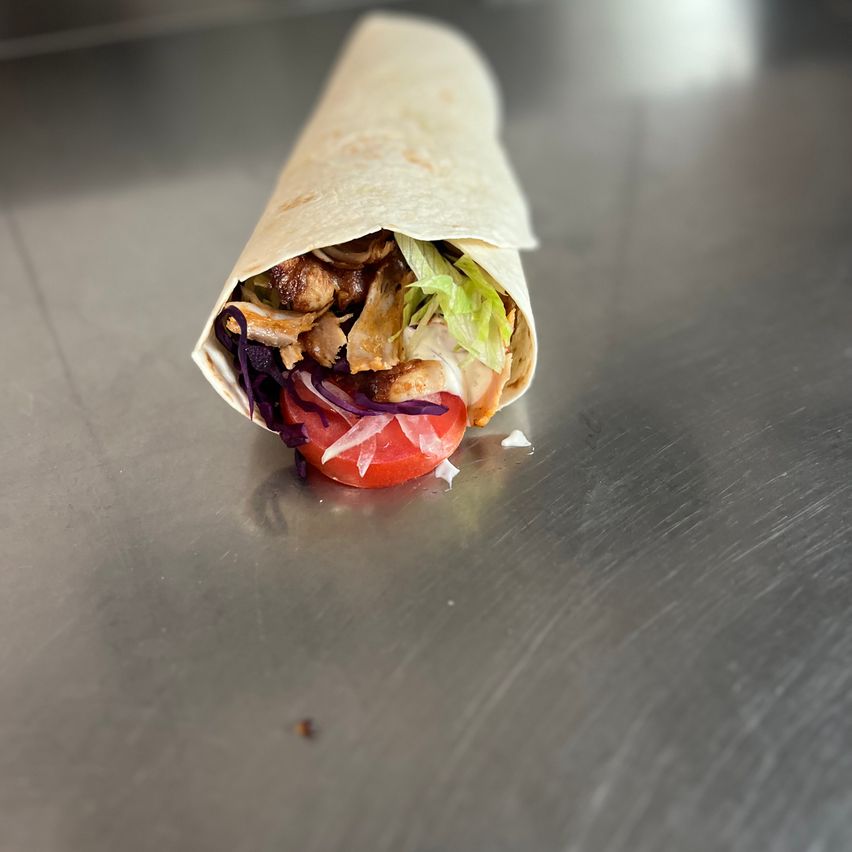 Ein Wrap ist geöffnet und zeigt eine Füllung aus Fleisch, Salat und einer Tomatenscheibe auf einer Metalloberfläche.