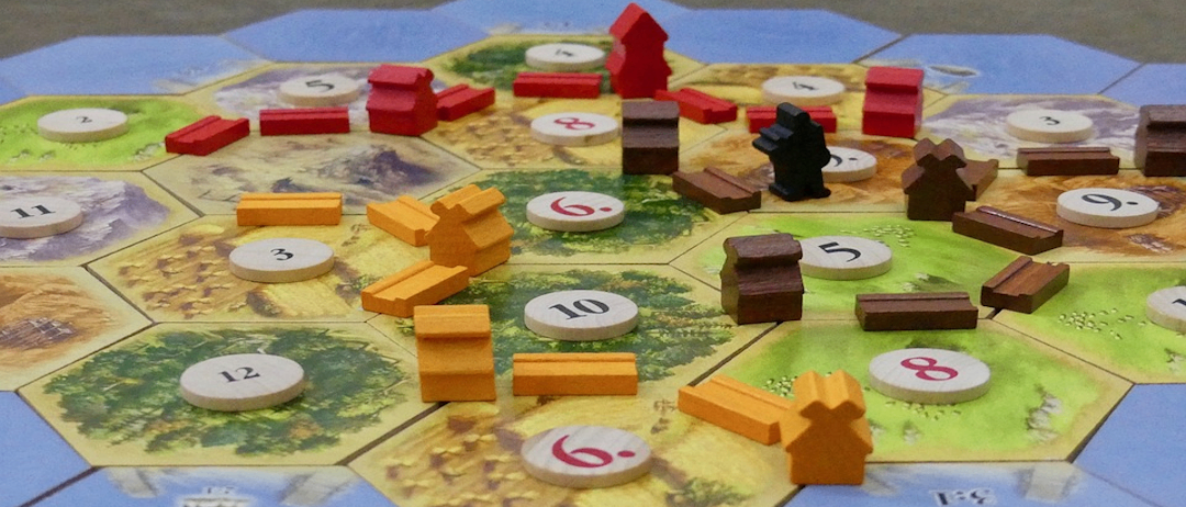 Ein Spielbrett für eine Tischplatte mit hexagonalen Kacheln, nummerierten Spielsteinen und verschiedenen Holzteilen, einschließlich Häusern und Brücken. Das Brett zeigt verschiedenfarbige Stücke und Spielsteine mit Zahlen.