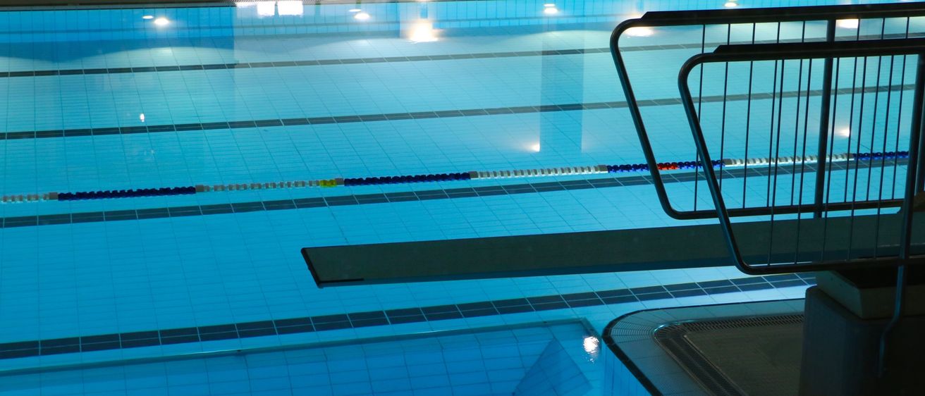 Ein Hallenbad mit blauen Fliesen und einer Metallhandlauf, reflektiert Licht und Wasser. Das Becken ist leer ohne Menschen.