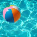 Ein farbenfroher Strandball schwimmt in einem klaren Pool, umgeben von welligem Wasser und Sonnenlichtreflexionen.