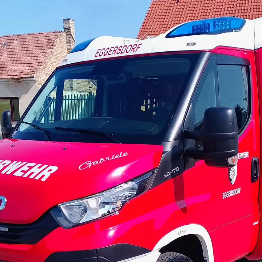 Ein roter und weißer Iveco-Feuerwehrwagen steht vor einem Haus mit rotem Dach. Der Wagen hat die Aufschrift Feuerwehr Eggersdoof an der Seite und ein Nummernschild mit dem Text FWI D313 MI.