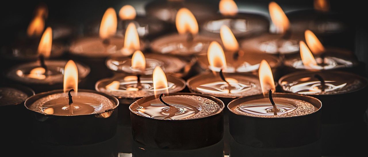 Eine Nahaufnahme von mehreren brennenden Kerzen in dunkler Umgebung, ihre Flammen flackern sanft und schaffen eine warme und intime Atmosphäre.