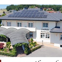 Gasthaus Kaufmann, ein weißes Gebäude mit Solarpanelen auf dem Dach, befindet sich in Wetzelsdorf 14, 8083 Jagerberg. Das Bild zeigt auch einen Teller mit Essen.