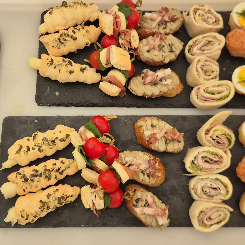 Two slate boards hold various canapes, including rolled sandwiches, skewered bites, and garnished bread slices. Some items feature tomatoes and cheese.