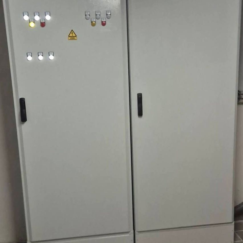 Two white electrical cabinets with multiple indicator lights and switches, one of which has a yellow triangle warning sign.