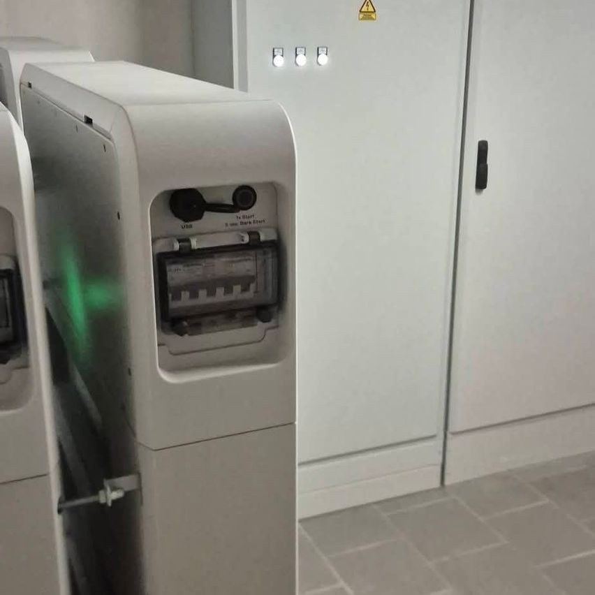 A white electrical panel with a green light is mounted on a wall, next to a door with a black handle.