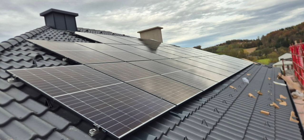 A roof with solar panels installed under a cloudy sky, with a chimney visible in the background.
