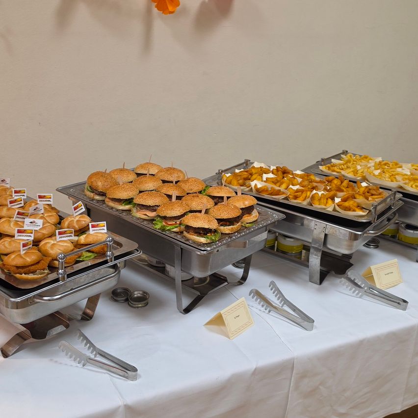 A table with multiple trays of food, including hamburgers, fries, and other snacks, arranged neatly with tongs and name tags.