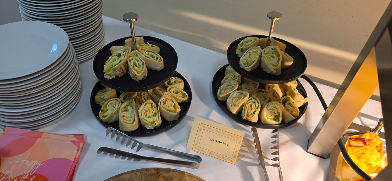 Two three-tiered stands filled with colorful vegetable wraps, each tier displaying a different roll shape. A yellow card with the text 'Vegetarischer Wrap' is placed next to one stand.