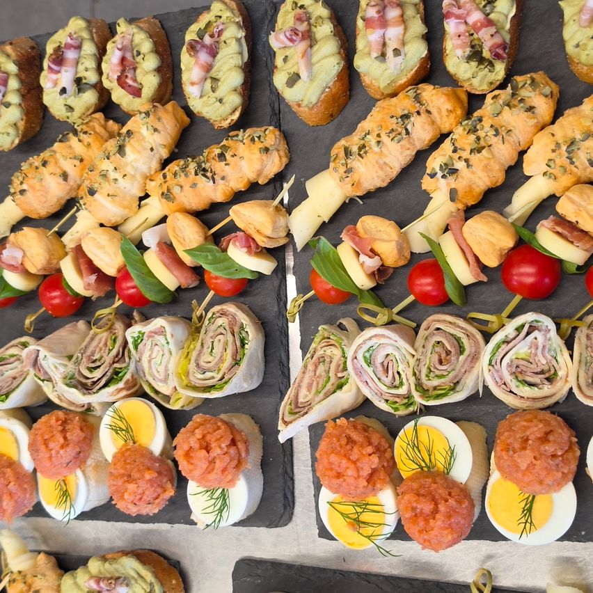 A variety of appetizers are displayed on a slate board, including avocado toast, cheese and meat skewers, and salmon roe with eggs.