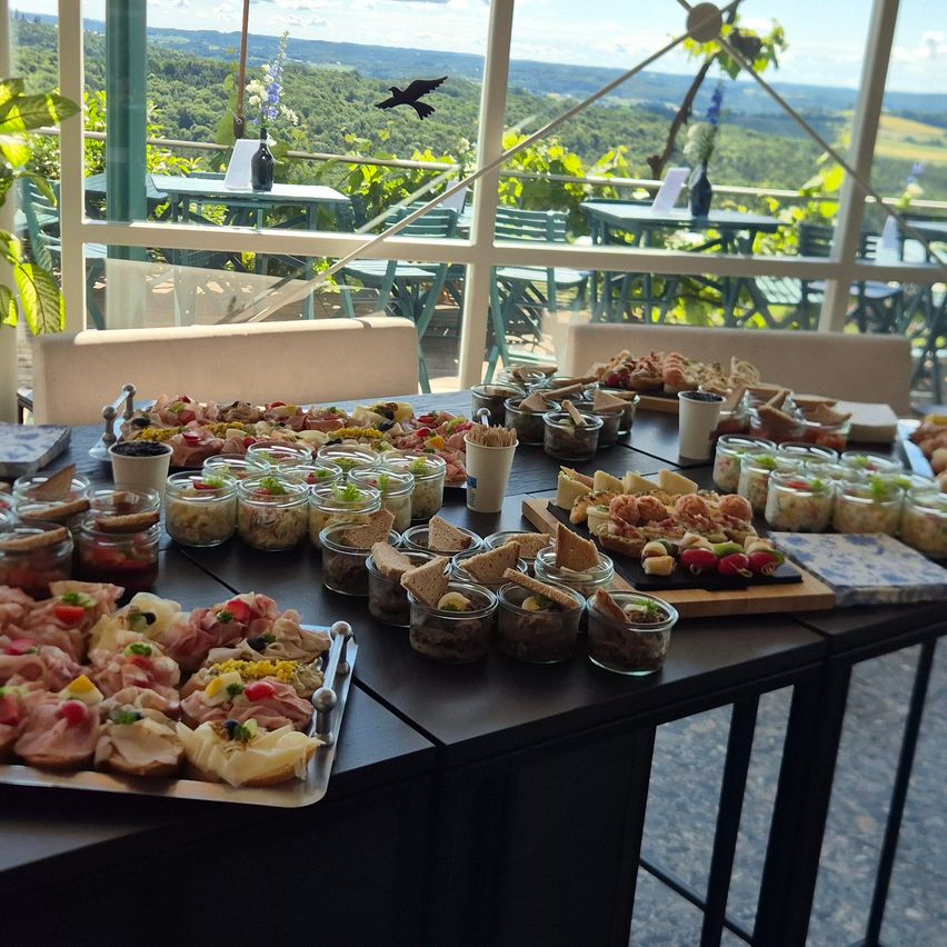 A table with a variety of dishes and snacks on it. The table is placed in a room with a view of a lush green valley.