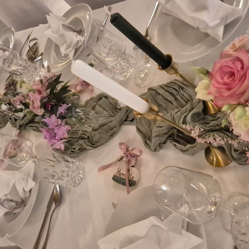 A table set for a special event with flowers, candles, and elegant tableware, including a decorative piece with the name 'Henriette'.