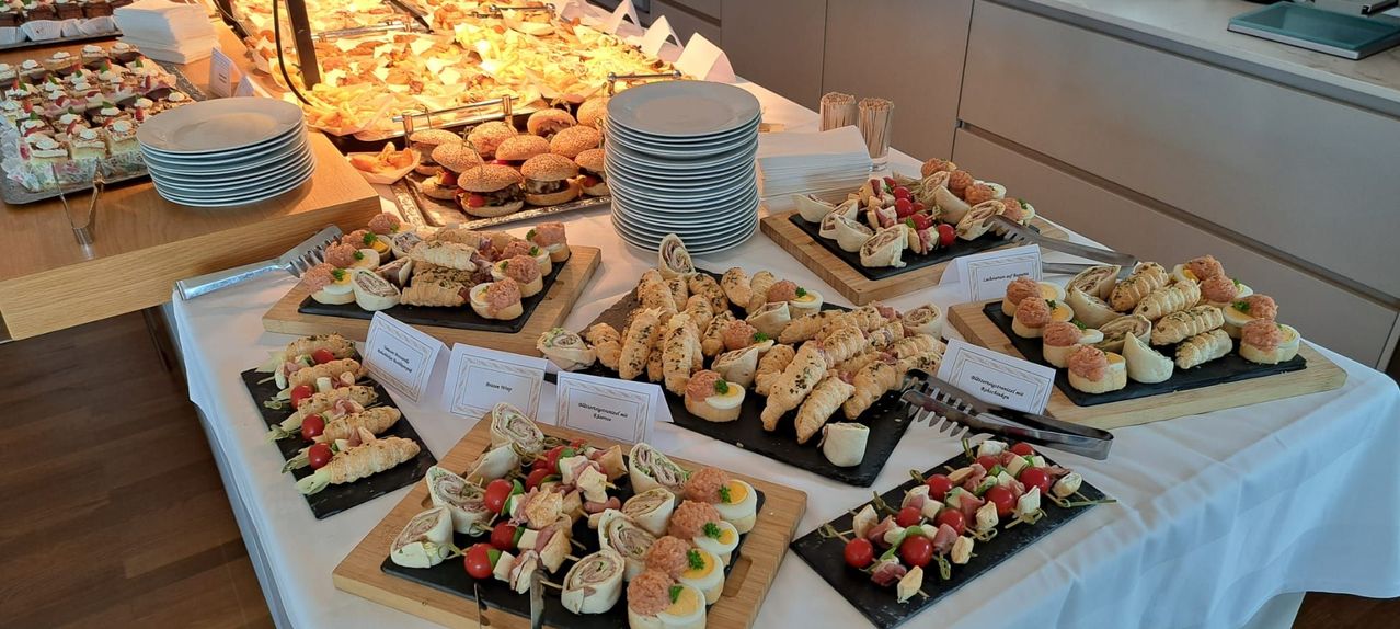 Ein Tisch ist mit einer Auswahl an Gourmet-Sandwiches gefüllt, darunter Wraps, Croissants und kleine Sandwiches, zusammen mit Stapeln von Tellern und Servietten.