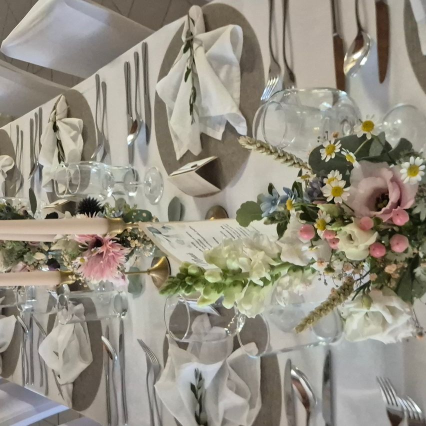 A long table set for a formal event with floral centerpieces, white napkins, and silverware. The table is covered with a white tablecloth.