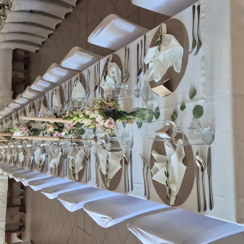 A long table set for a formal event with white tablecloth, floral centerpieces, and neatly folded napkins.