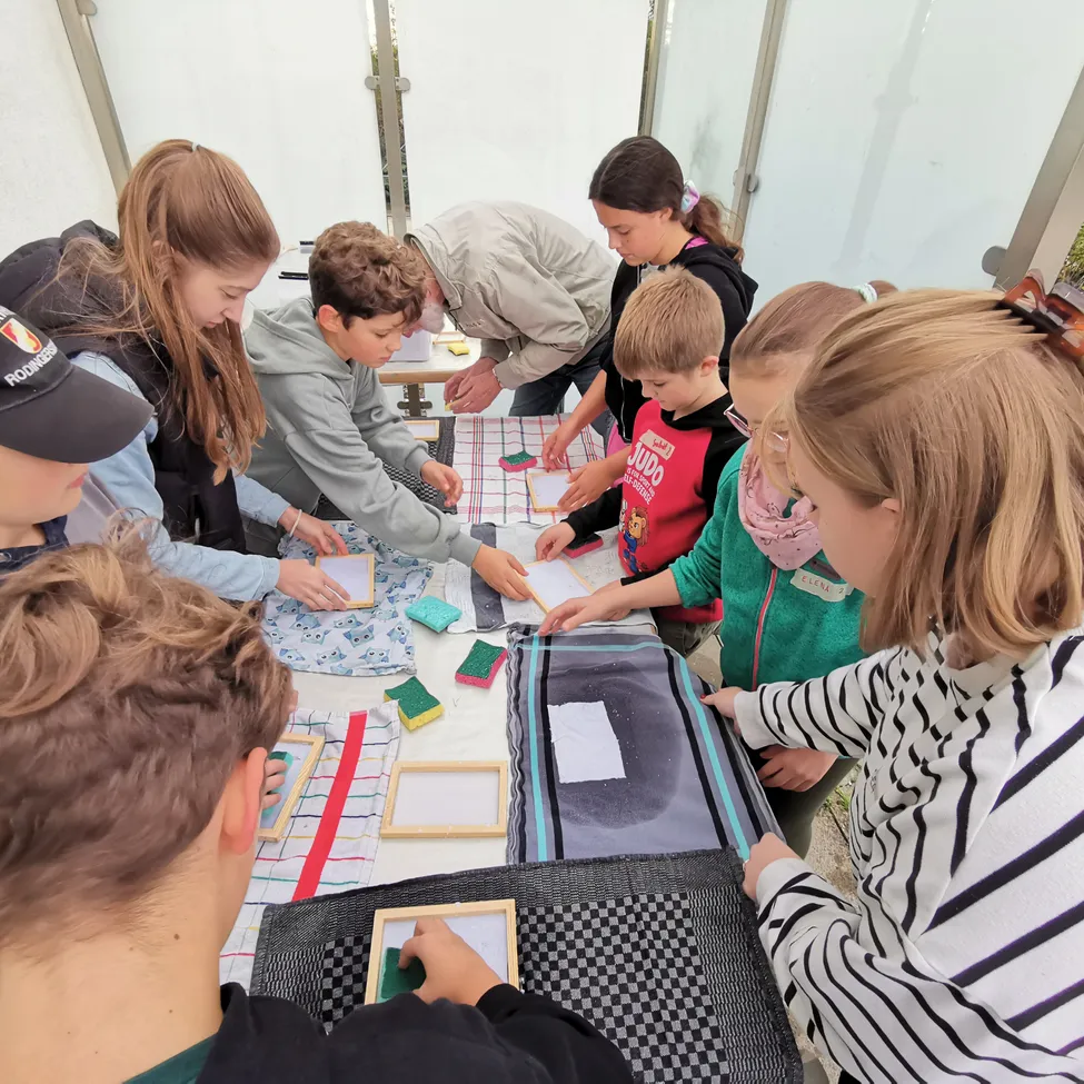 Eine Gruppe von Kindern arbeitet an einem Projekt am Tisch, wobei ein Kind auf ein Blatt Papier zeigt.