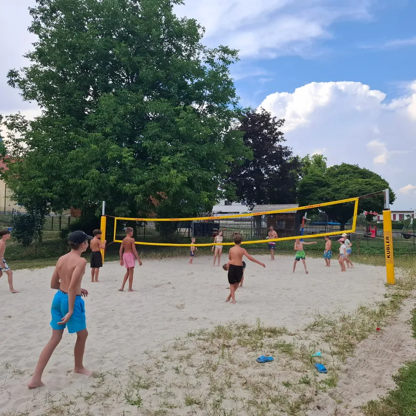 Eine Gruppe von Kindern spielt Volleyball auf einem sandigen Strand unter einem klaren blauen Himmel.