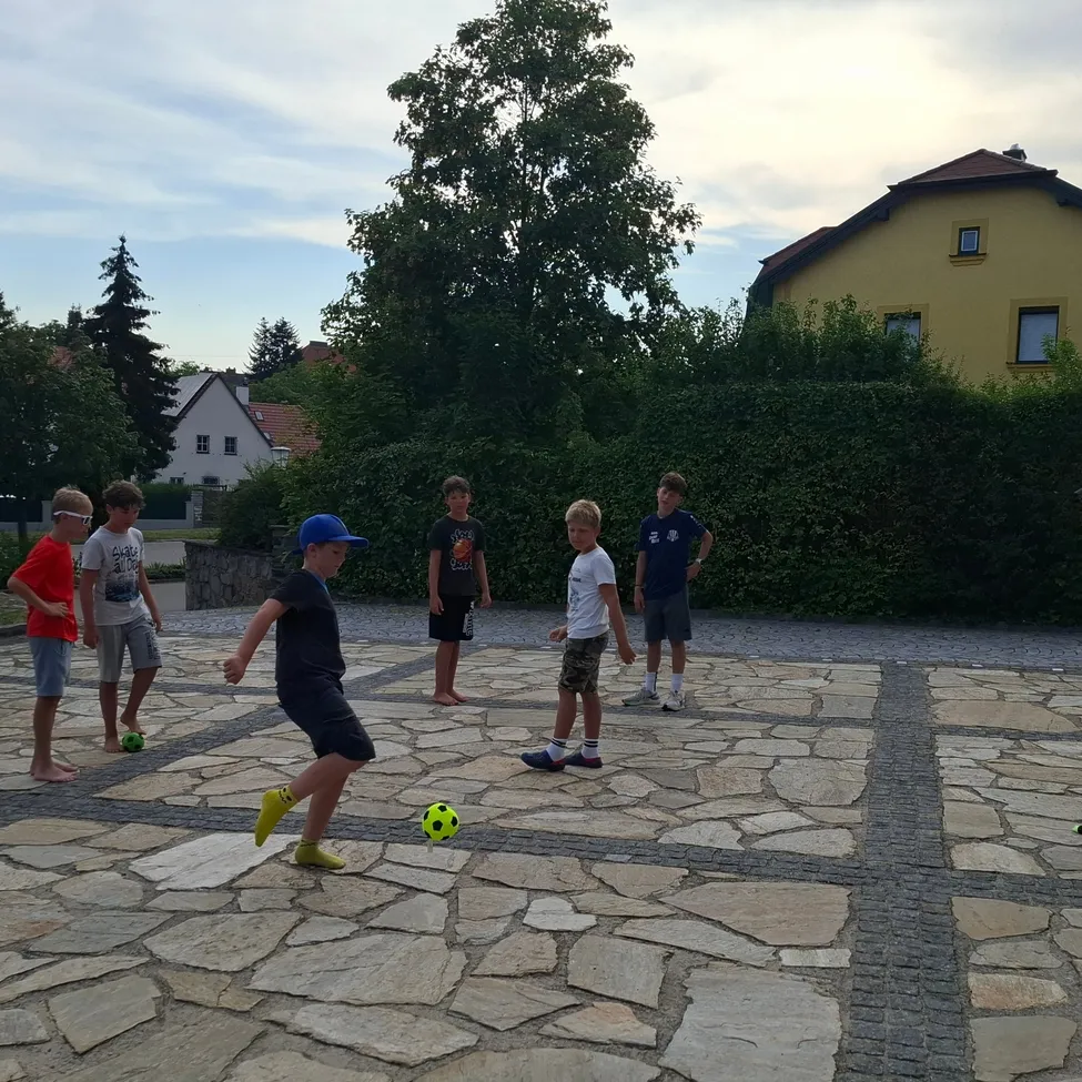 Eine Gruppe von Jungen spielt Fußball auf einem Steinpflaster. Ein Junge tritt den Ball, während andere zuschauen.