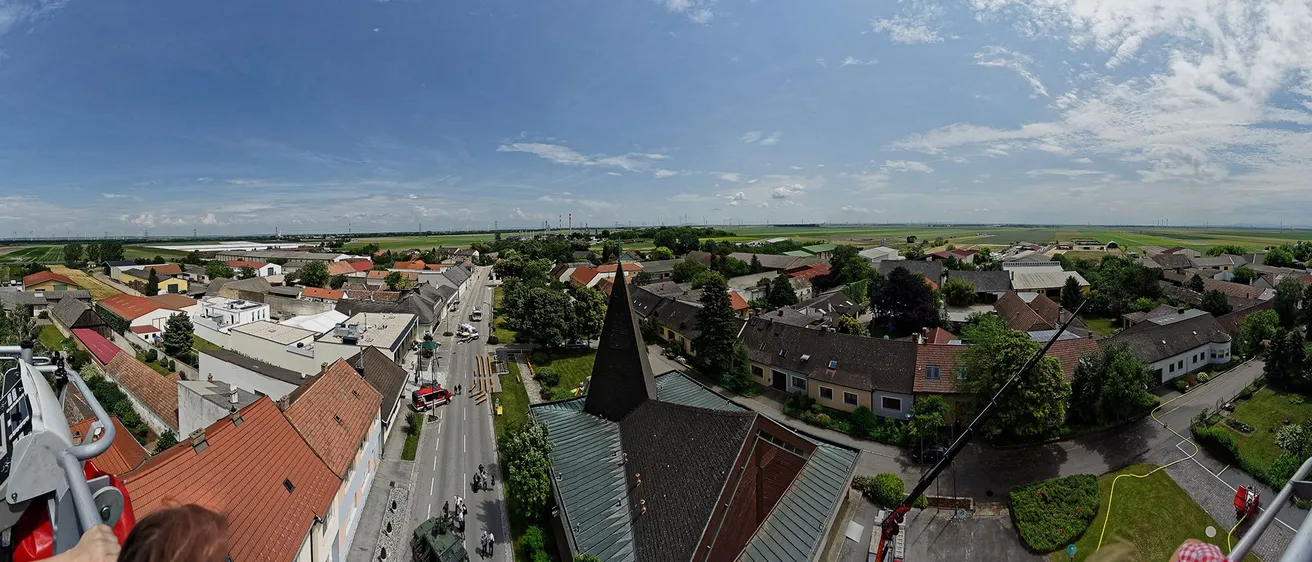 Luftaufnahme einer Stadt mit einer Turmkirche, einer Straße mit Fahrzeugen und einem Rettungsfahrzeug in der Nähe der Gebäude. Bäume und Pflanzen umgeben das Gebiet.