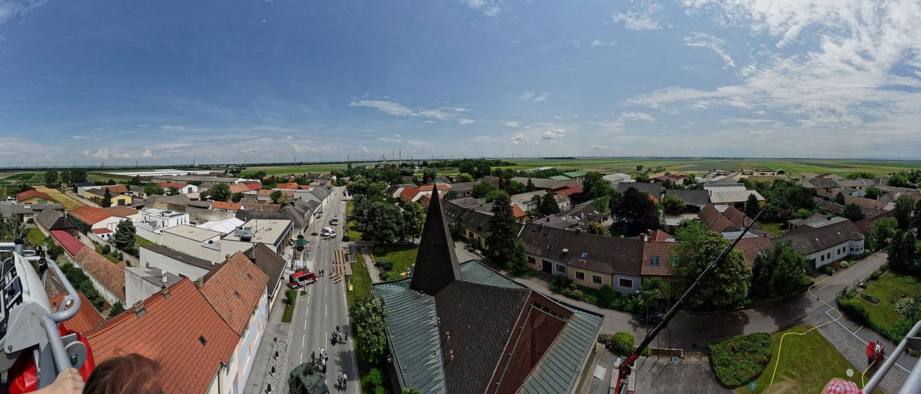 Luftaufnahme einer Stadt mit einer Turmkirche, einer Straße mit Fahrzeugen und einem Rettungsfahrzeug in der Nähe der Gebäude. Bäume und Pflanzen umgeben das Gebiet.